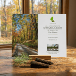 Memorial card with autumn forest scene and tree saplings on a wooden surface.