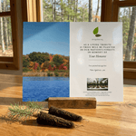 Memorial tree planting card with scenic lake and forest background on a wooden surface.