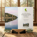Memorial card with nature-themed design on a wooden surface with a scenic background