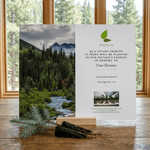 Memorial card for a living tribute with a scenic mountain and forest background, placed on a wooden surface.