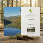 Memorial card with nature scene and tree sapling on a wooden surface