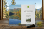Memorial plaque with a scenic view of a lake and trees, placed on a wooden surface with a window in the background.